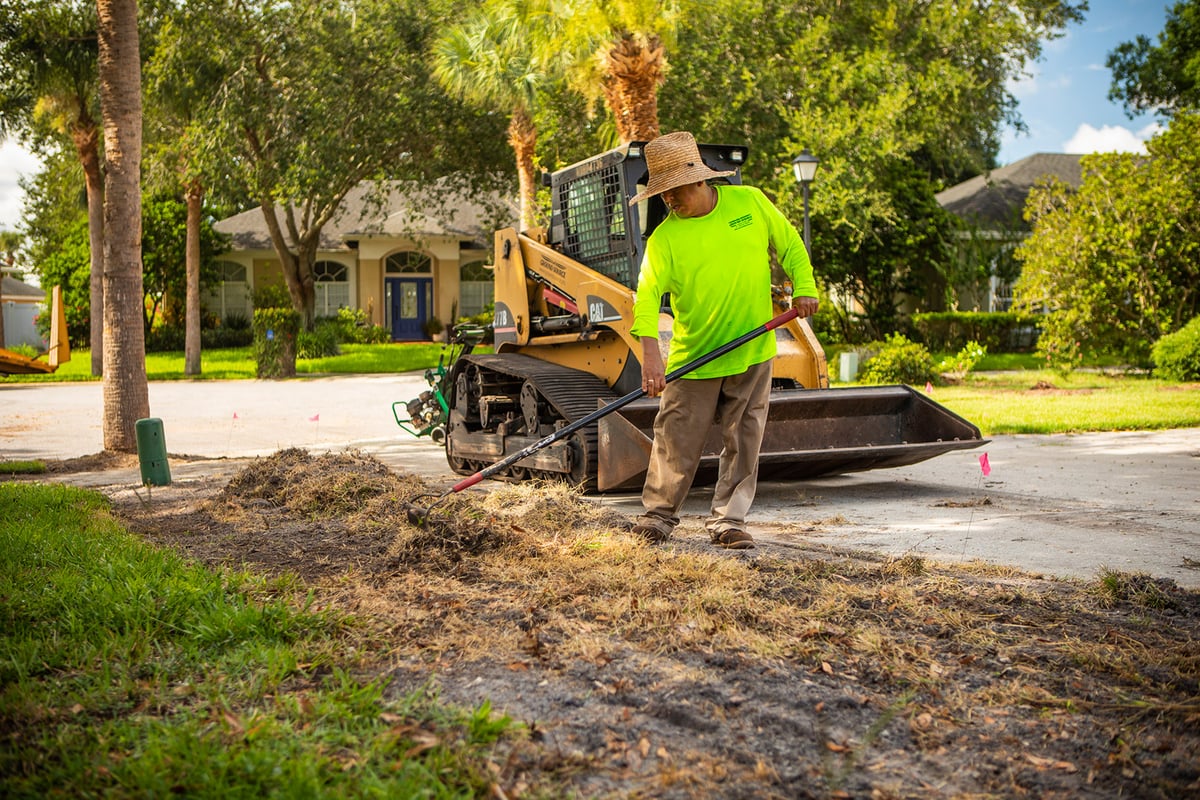 landscape professional rakes dead grass and weeds up from soil