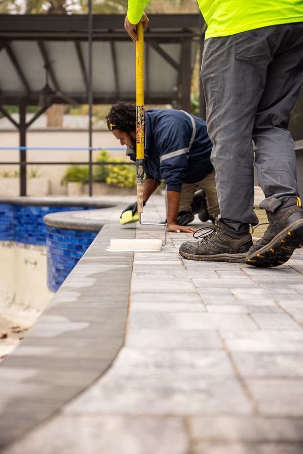 hardscape technicians sealing a paver border around a swimming pool