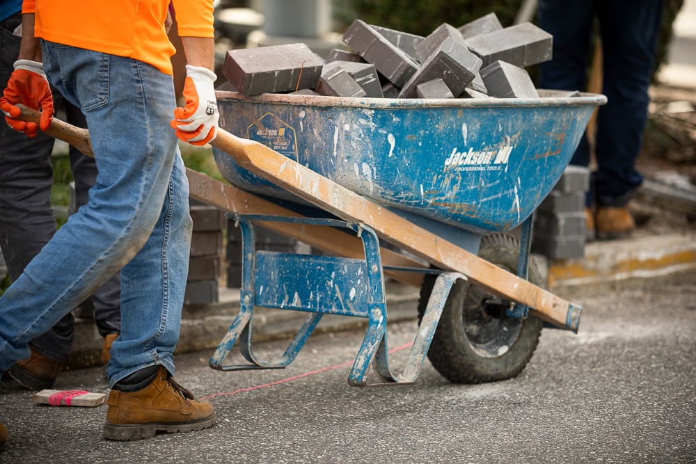 landscape installation team hauls pavers in wheelbarrow