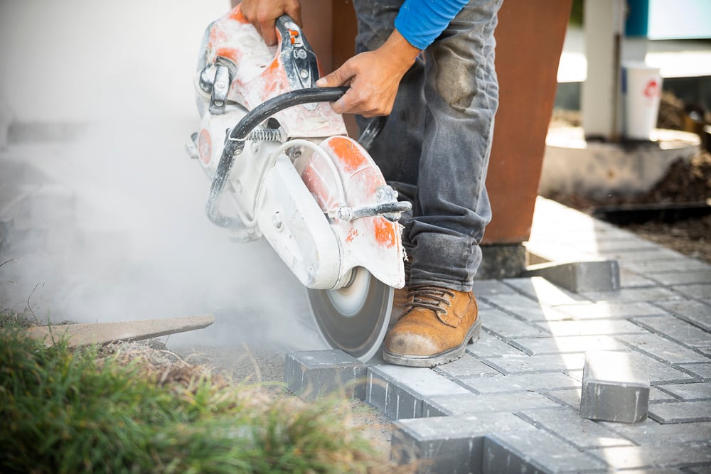 hardscape installation specialist cuts pavers with saw