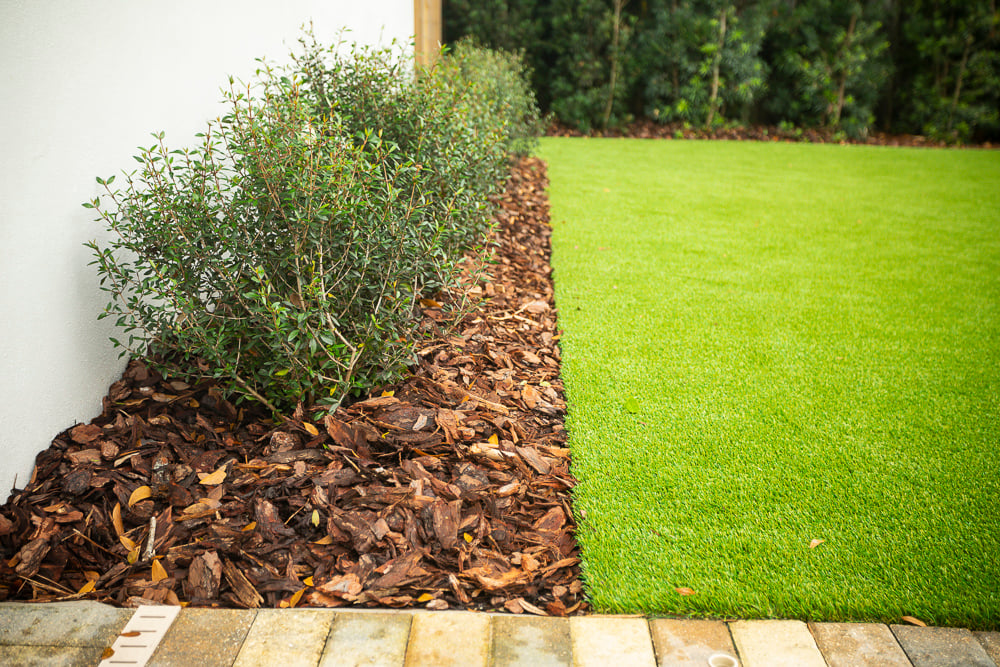 mulch in landscape bed with plantings near artificial turf