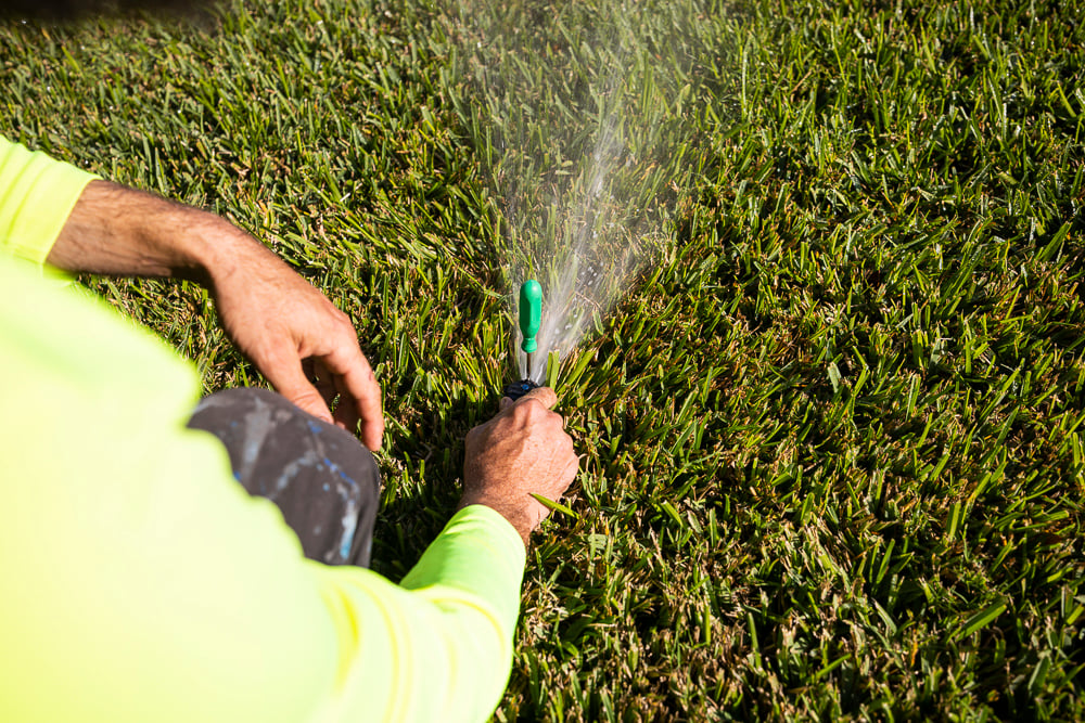 irrigation technician calibrating a lawn sprinkler system in a florida sod yard