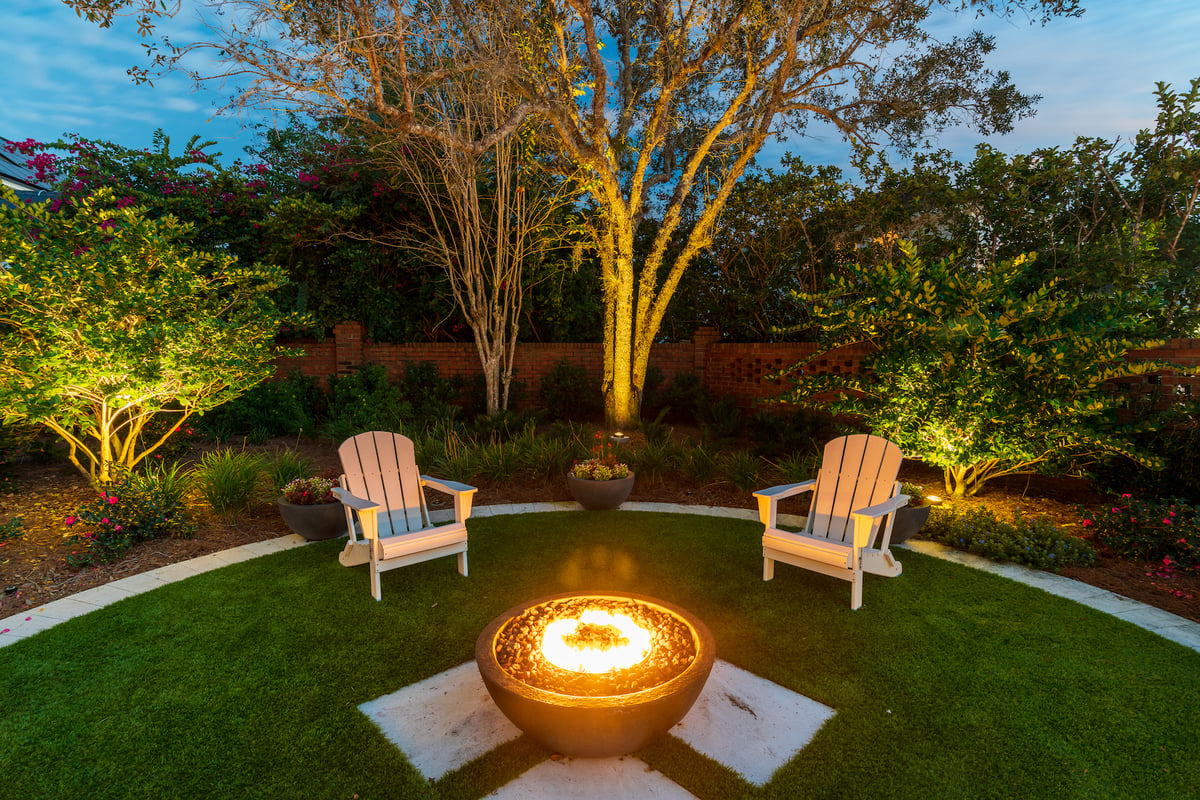 fire pit and seating area with trees lit by landscape lighting