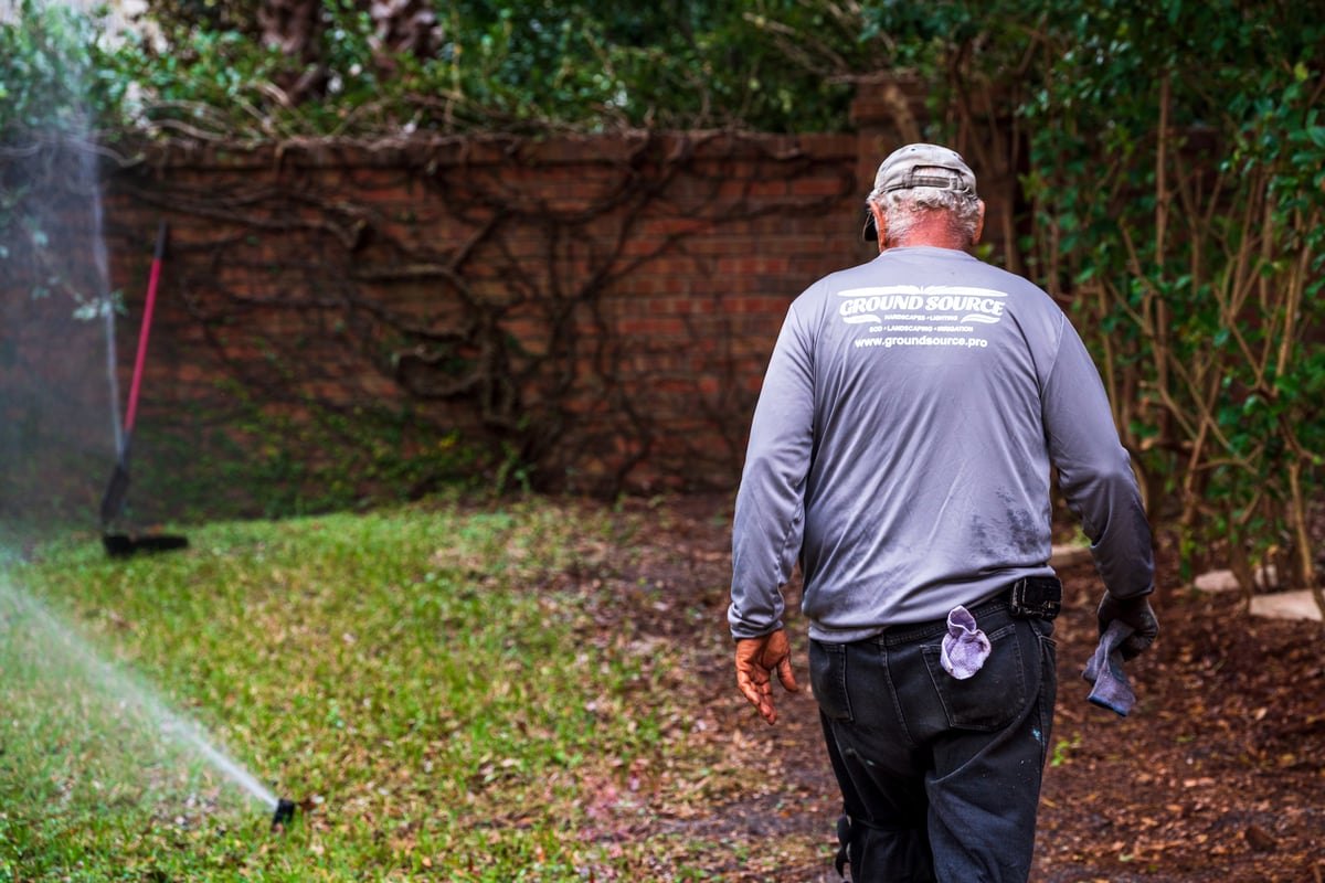 irrigation technician walks in back yard inspecting sprinklers