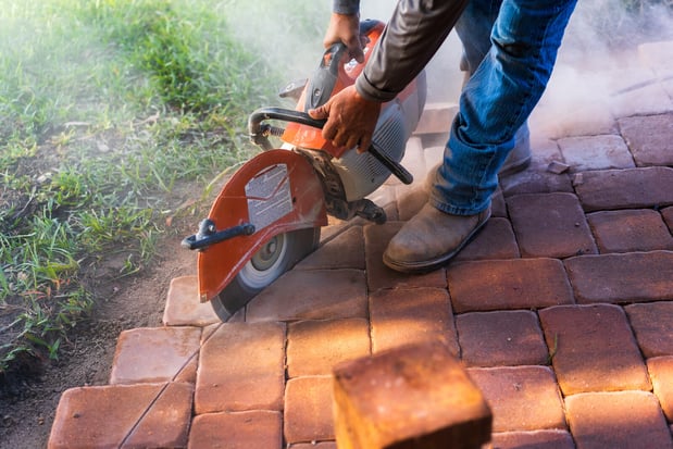 landscape installation team member cutting concrete patio pavers