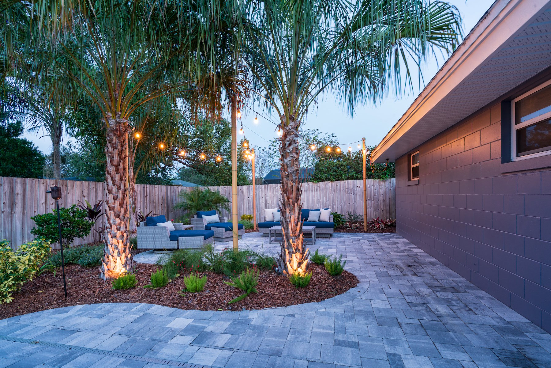 landscape lighting on trees in small backyard with patio and plantings