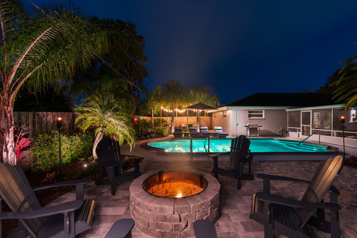 firepit on paver patio around pool with landscape lighting and plantings