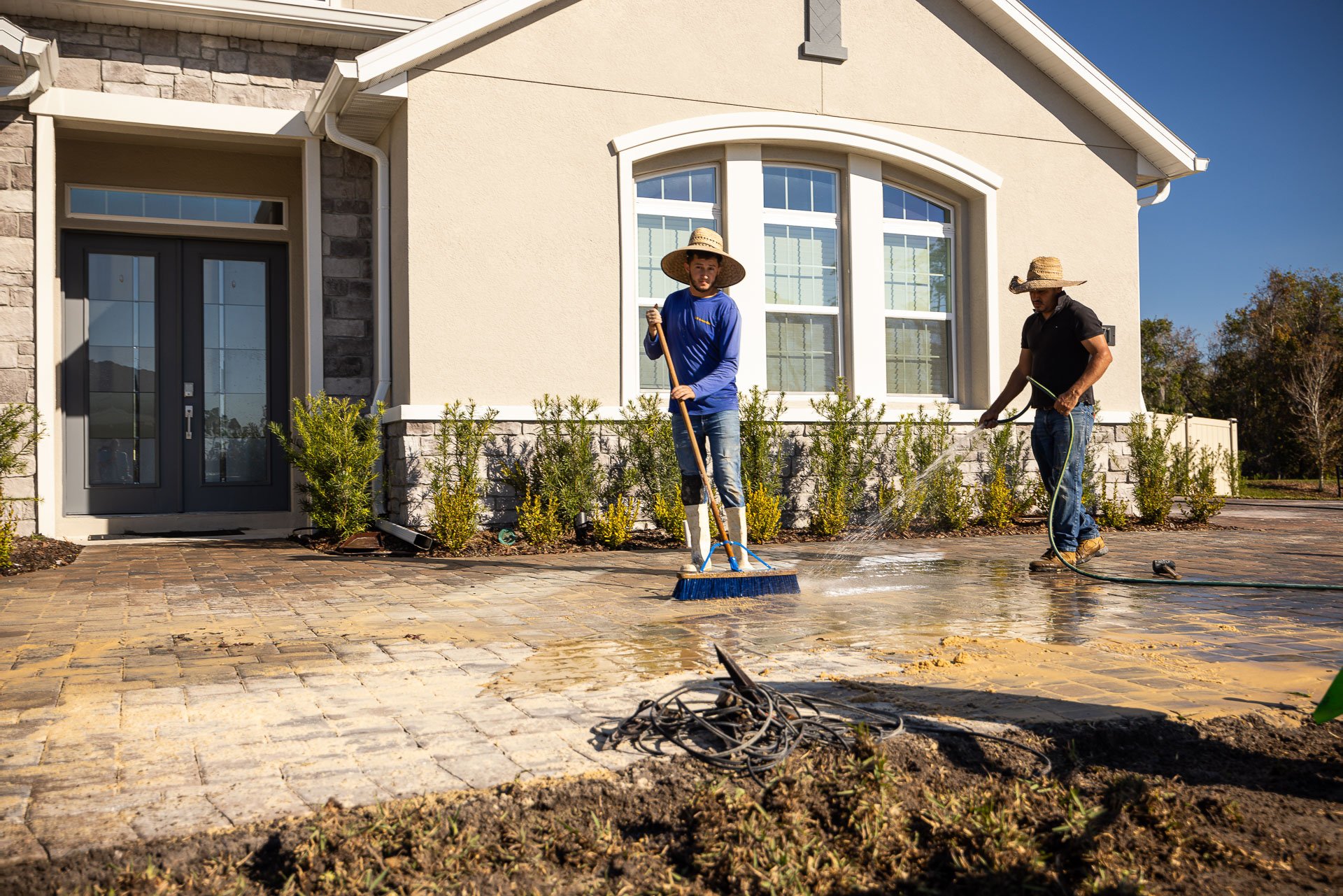 paver installers sweeping sand into the joints of a new paver driveway