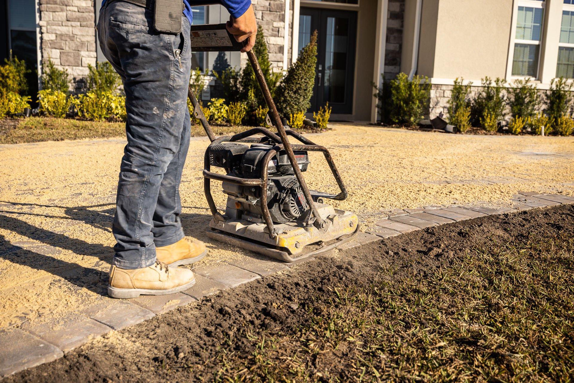 hardscape technician running a plate compactor over a paver driveway