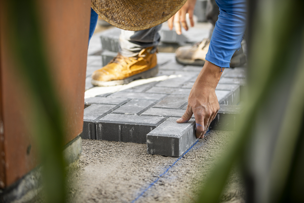 landscape professional lays brick pavers on base